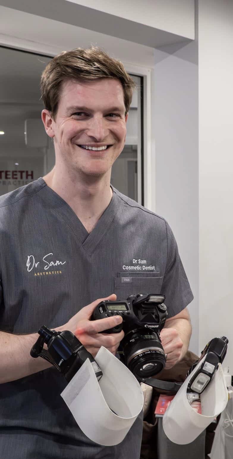 Dr Sam Cope holding a Canon DSLR with a dual-flash macro setup in clinical scrubs